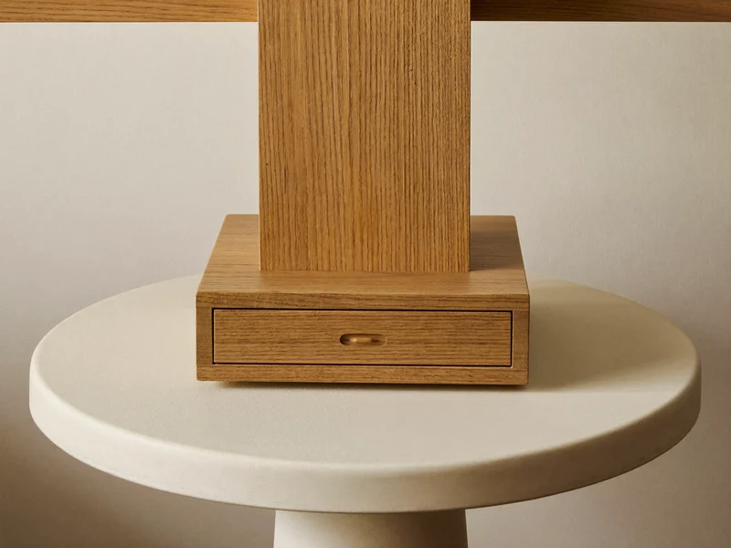 Monitorerhöhung aus Eiche mit kleiner Schublade auf hellem Sockel vor neutraler Wand.