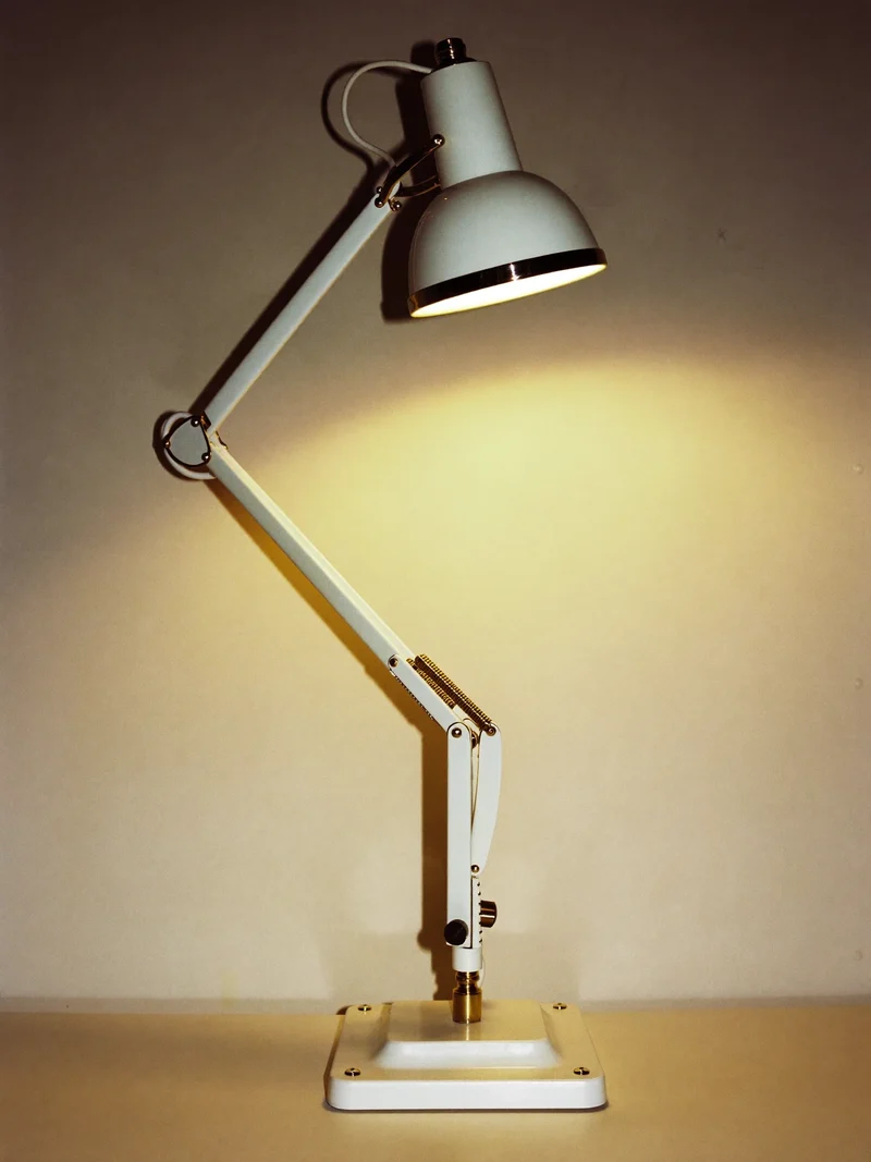 Verstellbare Tischleuchte aus Messing und Weiss mit warmem Lichtschein an der Wand.