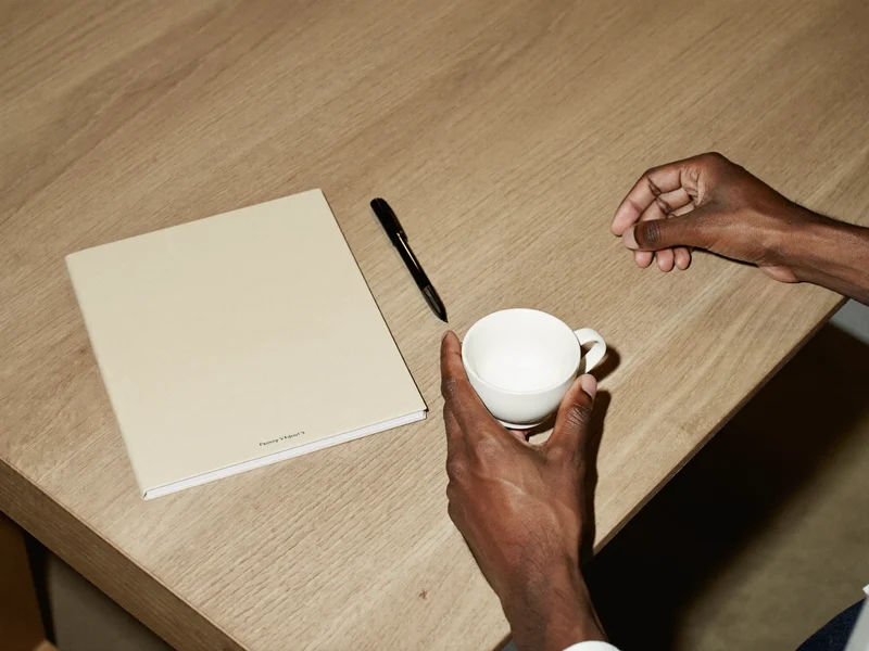 Hände ordnen Notizbuch, Keramiktasse und Stift auf einem aufgeräumten Schreibtisch.