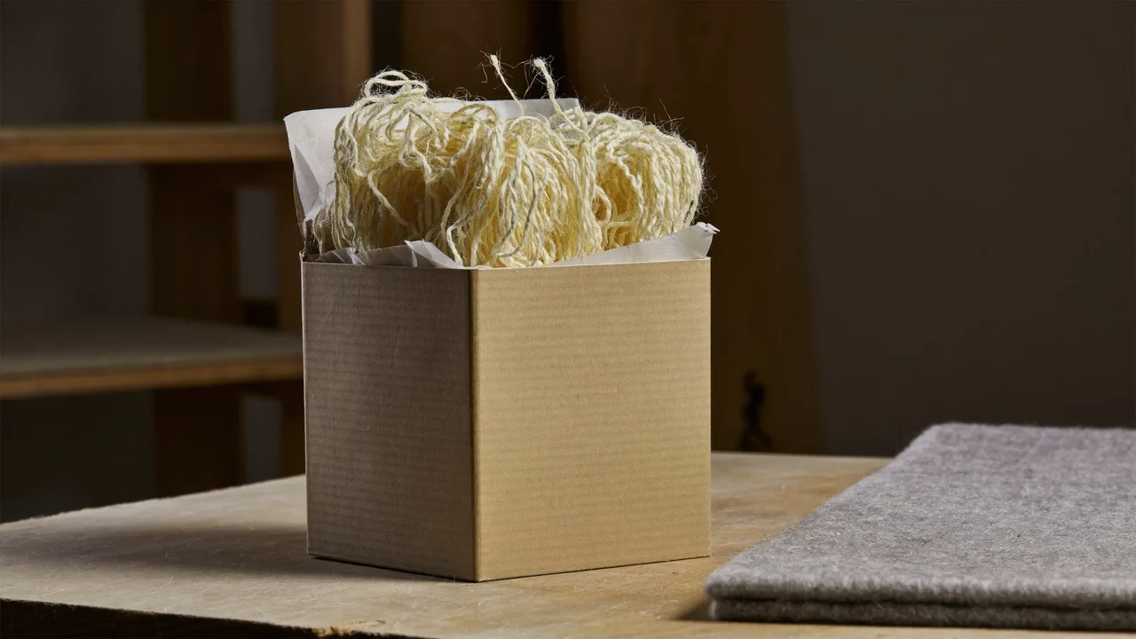 Unbedruckte Kartonverpackung mit Holzwolle und Filzunterlage auf einem Werkstatttisch, illustrativ.
